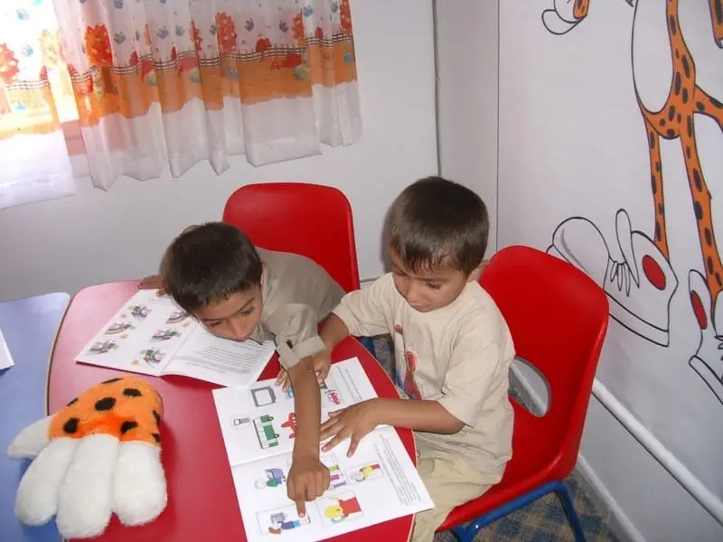 Okuma odasında kırmızı masada kitap okuyan iki çocuk